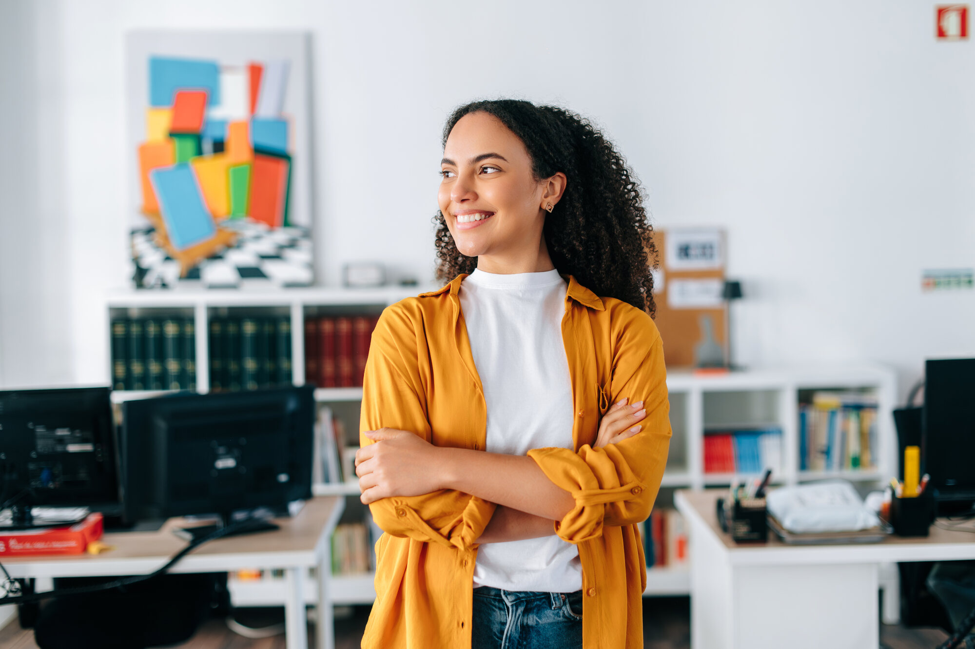 Smiling student in a mustard shirt standing in a bright office